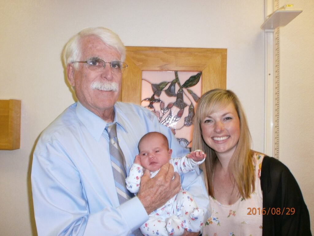 A picture of Dr. Steve Jimerson MD OBGYN holding a baby he delivered with the post pregnant mother he delivered for